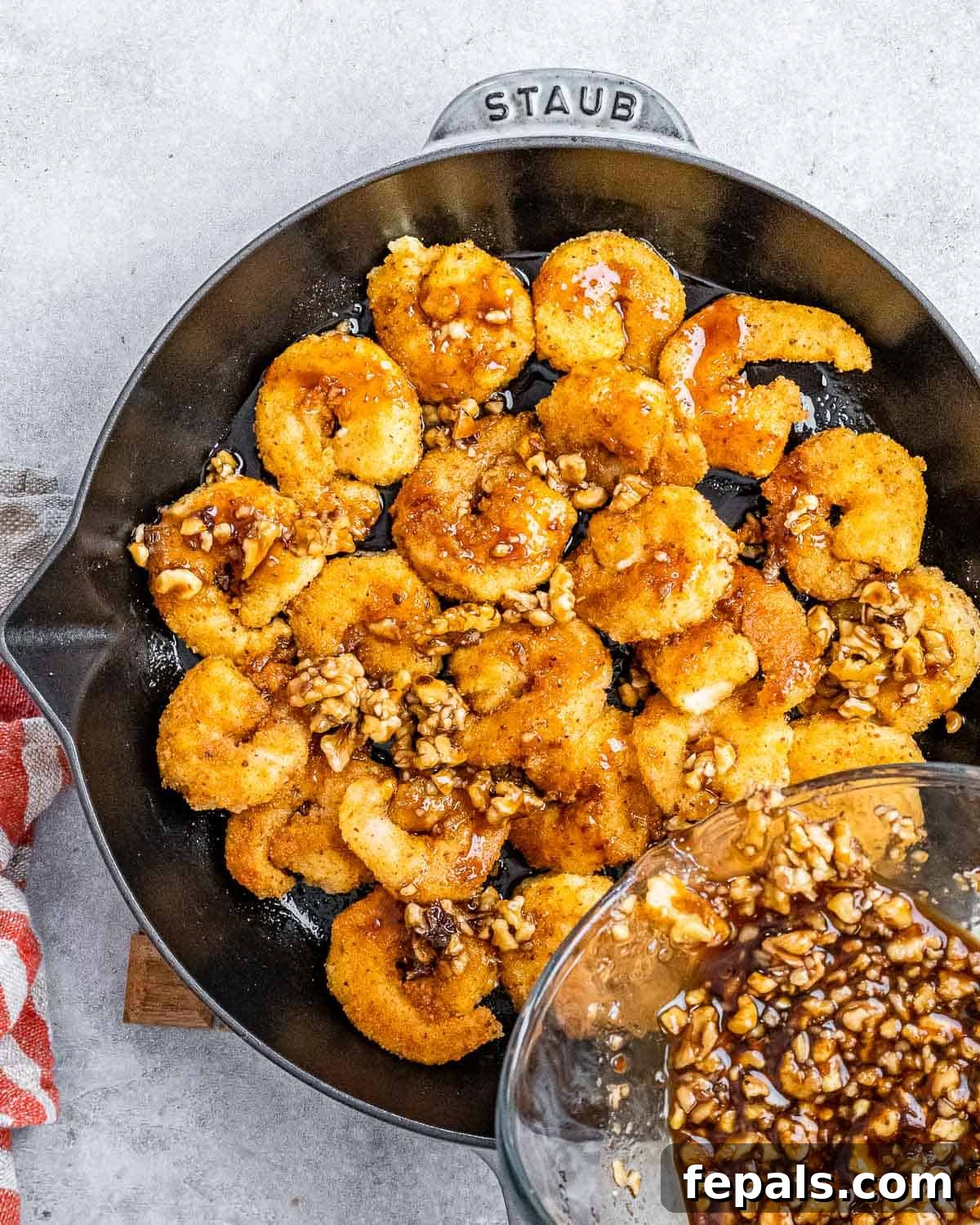Cooked crispy shrimp in a skillet being tossed with the honey-walnut sauce, ensuring every piece is coated.