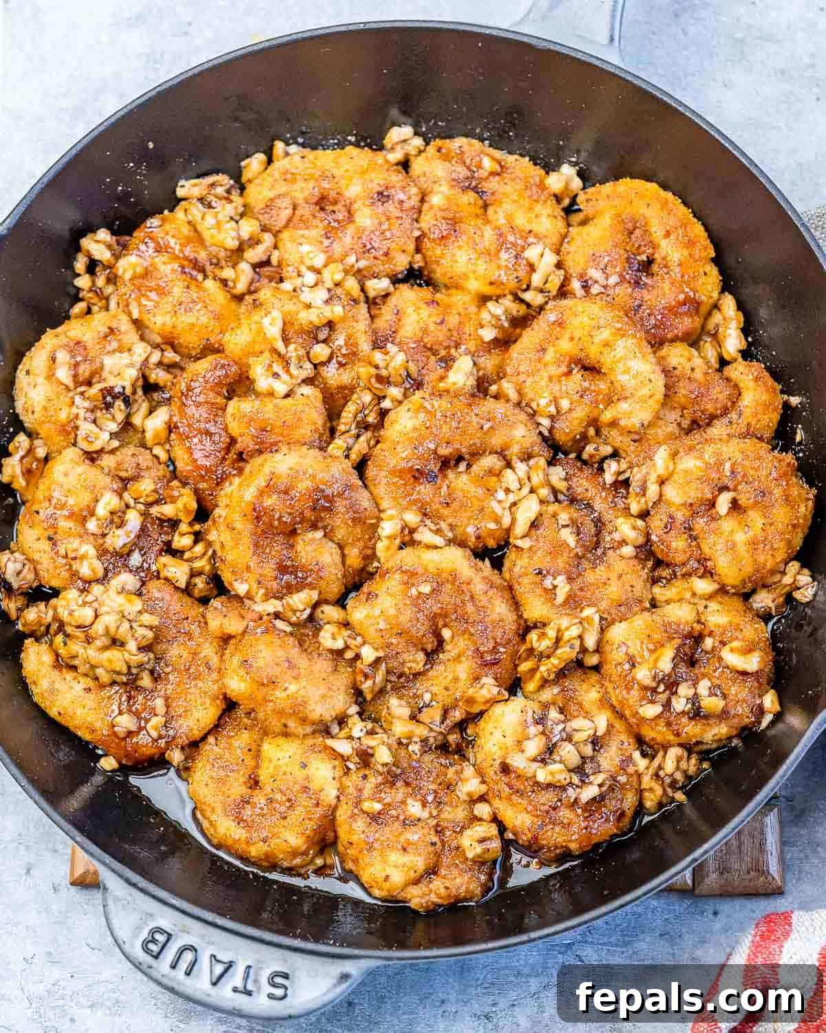A close-up shot of crispy honey walnut shrimp sizzling in an iron skillet, glistening with sauce and walnuts.