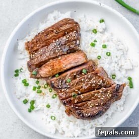 Sweet and Savory Teriyaki Steak 11 A round white plate with white rice topped with sliced teriyaki steak garnished with chopped green onions and sesame seeds.