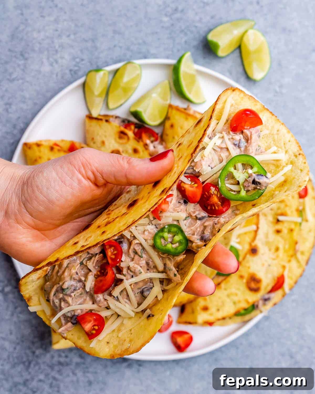 Effortless Flavorful Shredded Chicken Tacos 11 A fully assembled chicken taco filled with shredded chicken, beans, and toppings, placed on a plate with lime wedges.