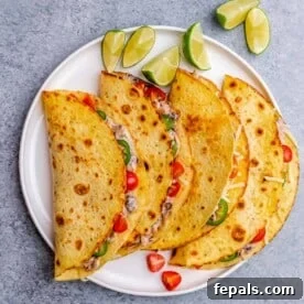 A close-up of four folded chicken tacos garnished with cherry tomatoes, jalapeños, and lime wedges.