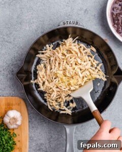 Effortless Flavorful Shredded Chicken Tacos 7 Shredded chicken being sautéed in a black skillet with a white spatula.