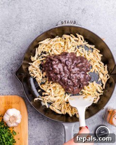 Effortless Flavorful Shredded Chicken Tacos 8 A skillet with shredded chicken and mashed black beans being mixed together with a spatula.