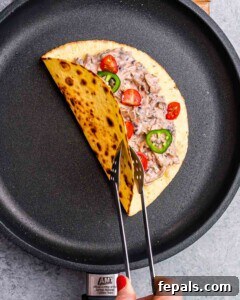 Effortless Flavorful Shredded Chicken Tacos 9 A single taco in a skillet being toasted and flipped with tongs.