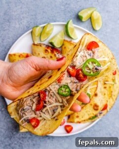 Effortless Flavorful Shredded Chicken Tacos 10 A fully assembled chicken taco filled with shredded chicken, beans, and toppings, placed on a plate with lime wedges.