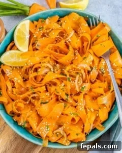 A round blue plate with sliced carrot salad and lemon wedges on the left side of the salad.