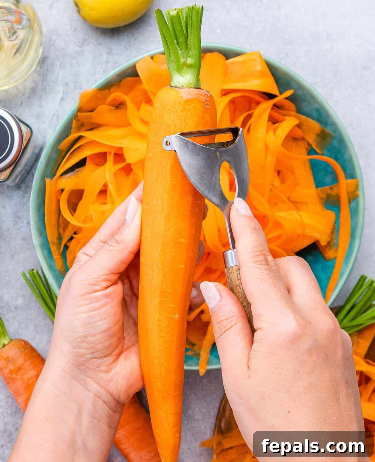 Viral Carrot Salad Sensation 5 A hand using a vegetable peeler to peel thin ribbons of carrot into a blue bowl.