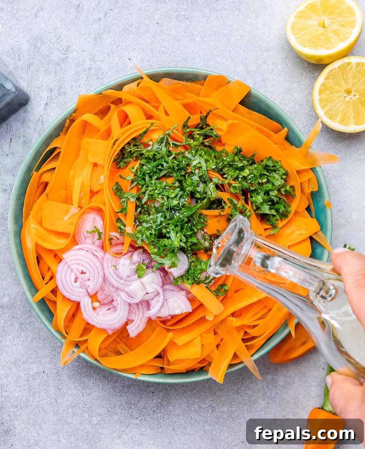 Viral Carrot Salad Sensation 6 Chopped shallots and cilantro being added over the shredded carrot salad in a bowl, followed by a drizzle of dressing.