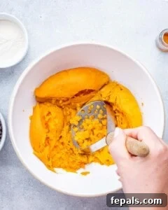cooked sweet potatoes in a bowl being mashed with a masher.
