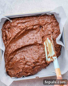 brownie batter is spread in a pan lined up with parchment paper.