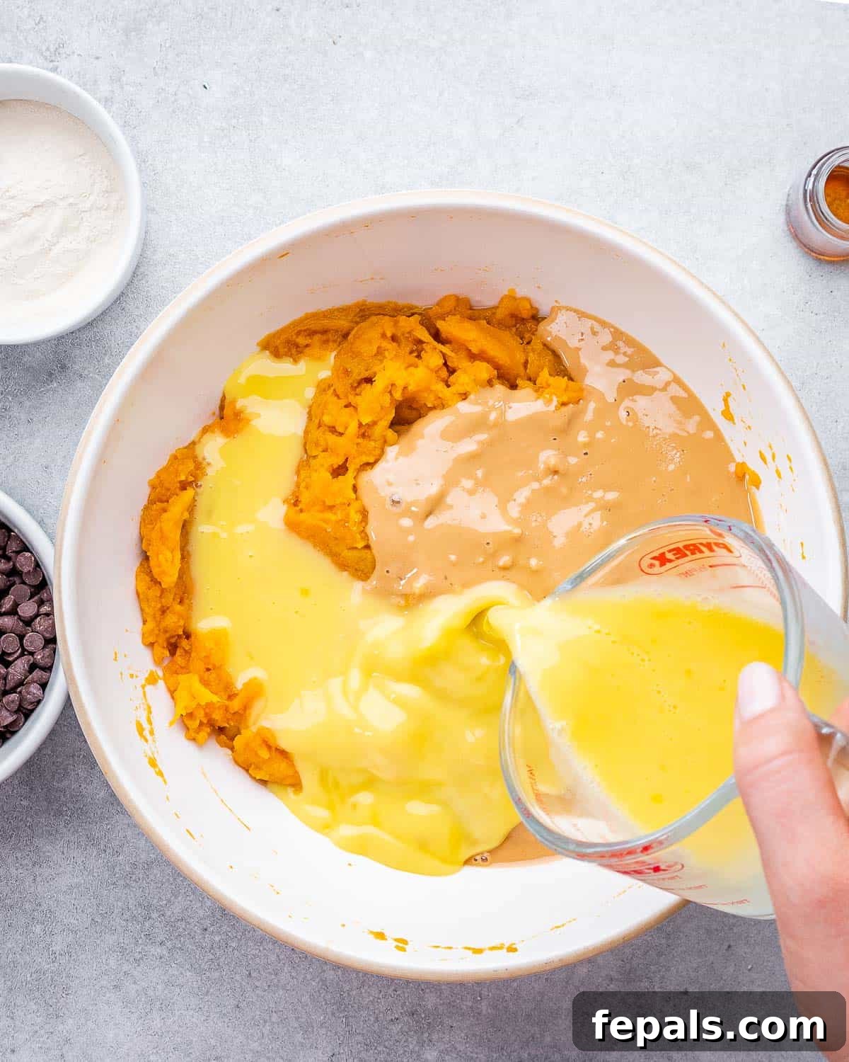 Beaten eggs being poured over a mixture of mashed sweet potatoes and peanut butter in a round mixing bowl, ready to be combined.
