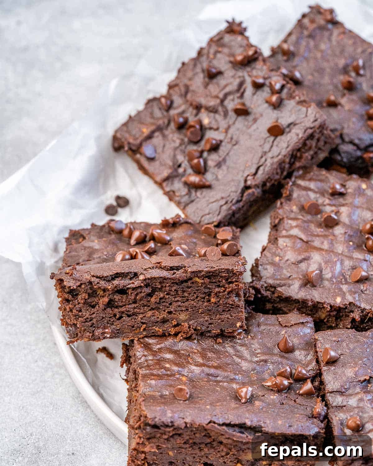 Several square sweet potato brownies neatly arranged on a pristine white plate, showcasing their inviting texture.