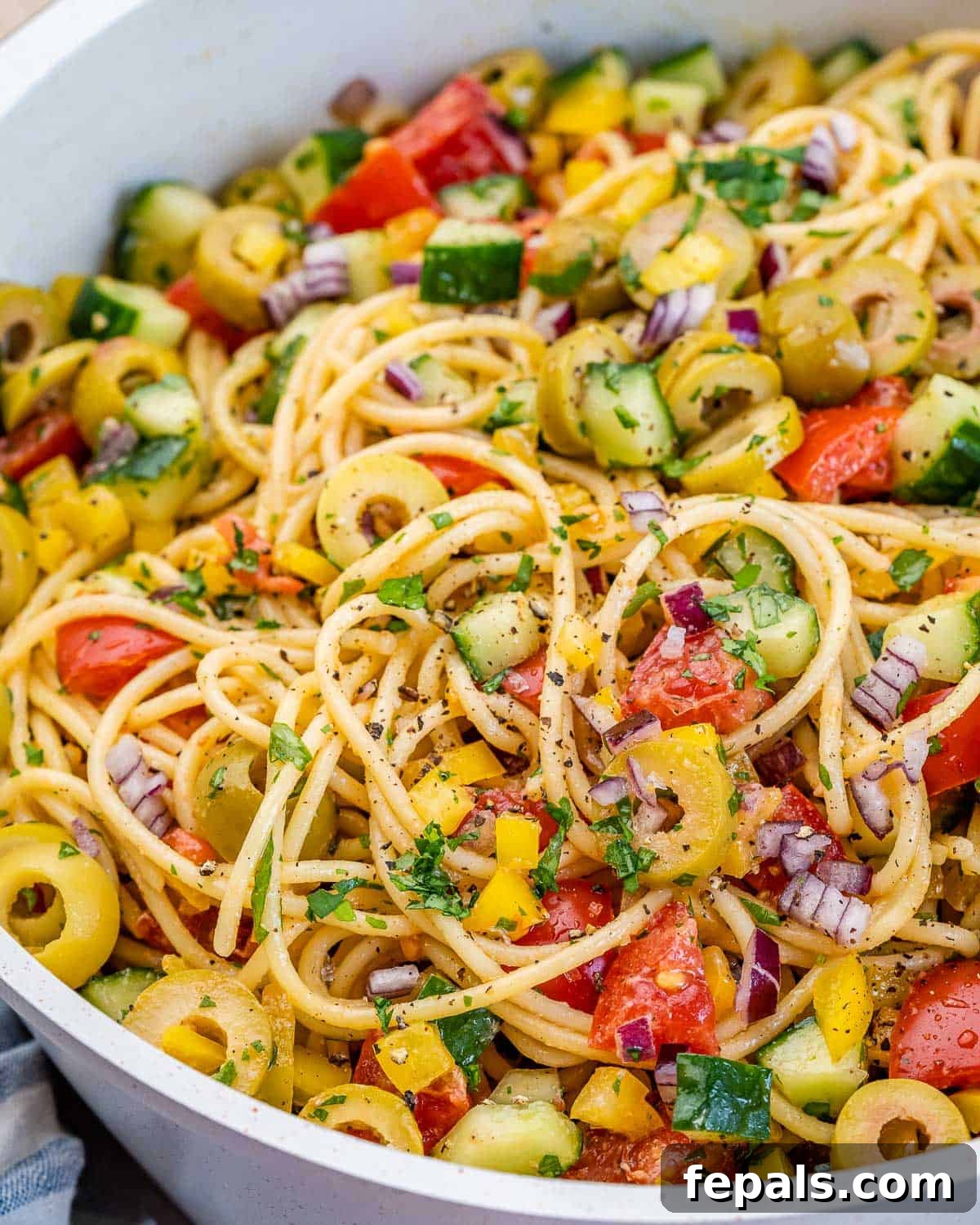 Refreshing Spaghetti Salad 11 A close-up shot of a vibrant spaghetti salad served in a pristine white dish, meticulously arranged to showcase its rich array of chopped vegetables and long spaghetti strands.