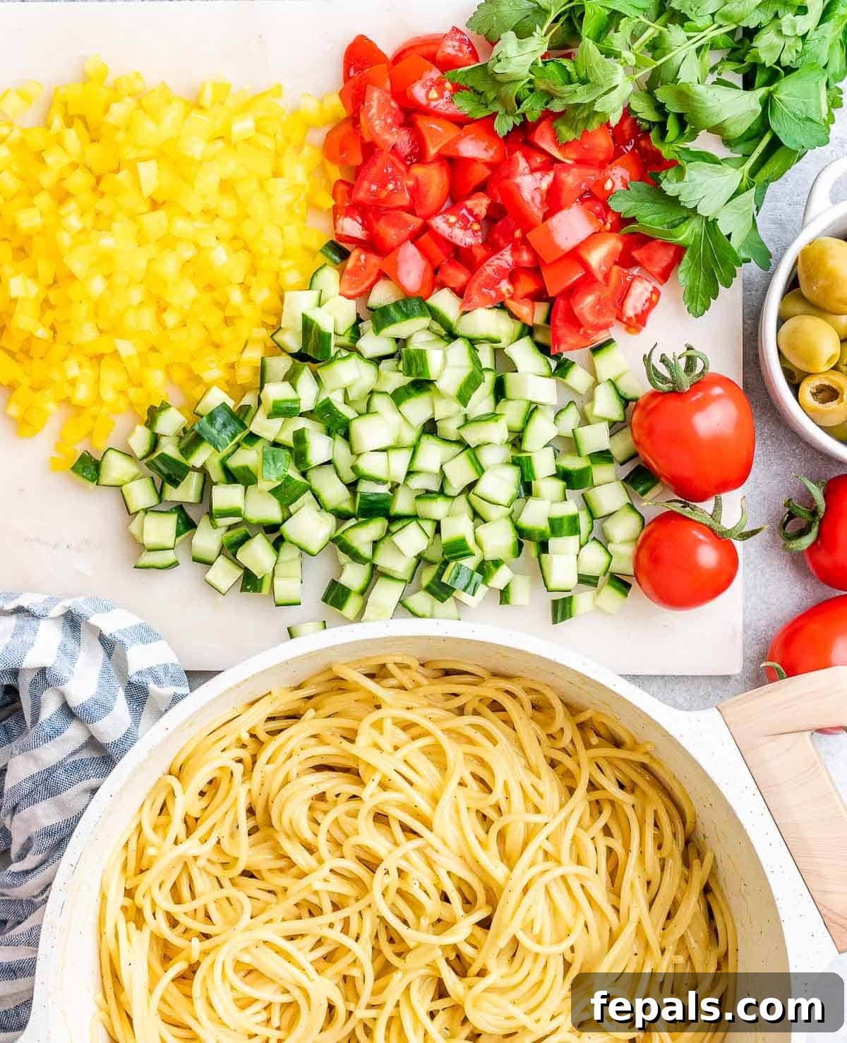 Refreshing Spaghetti Salad 4 A large bowl filled with perfectly cooked spaghetti, next to a platter showcasing an array of freshly chopped vegetables including red onion, tomatoes, and bell peppers, all ready to be combined into a refreshing salad.