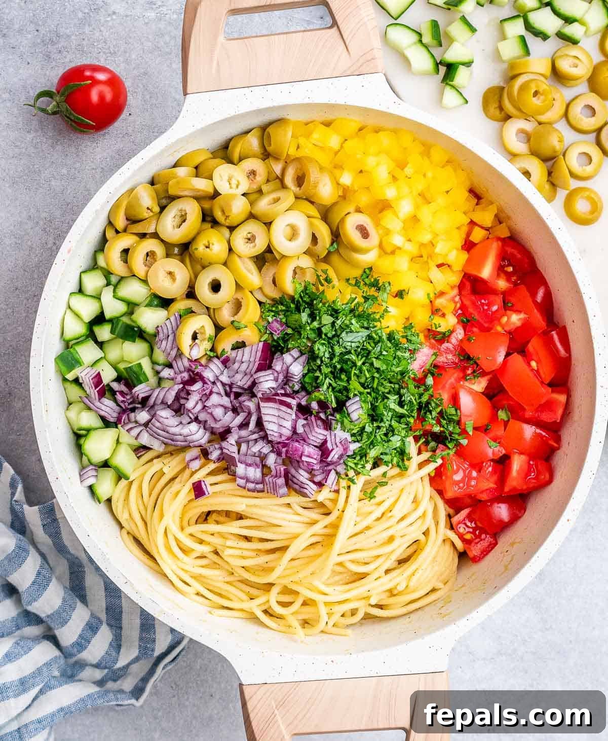 Refreshing Spaghetti Salad 7 A large, inviting round bowl filled with spaghetti mixed with a colorful array of freshly chopped vegetables including diced tomatoes, cucumbers, bell peppers, red onion, and sliced green olives, ready to be served.