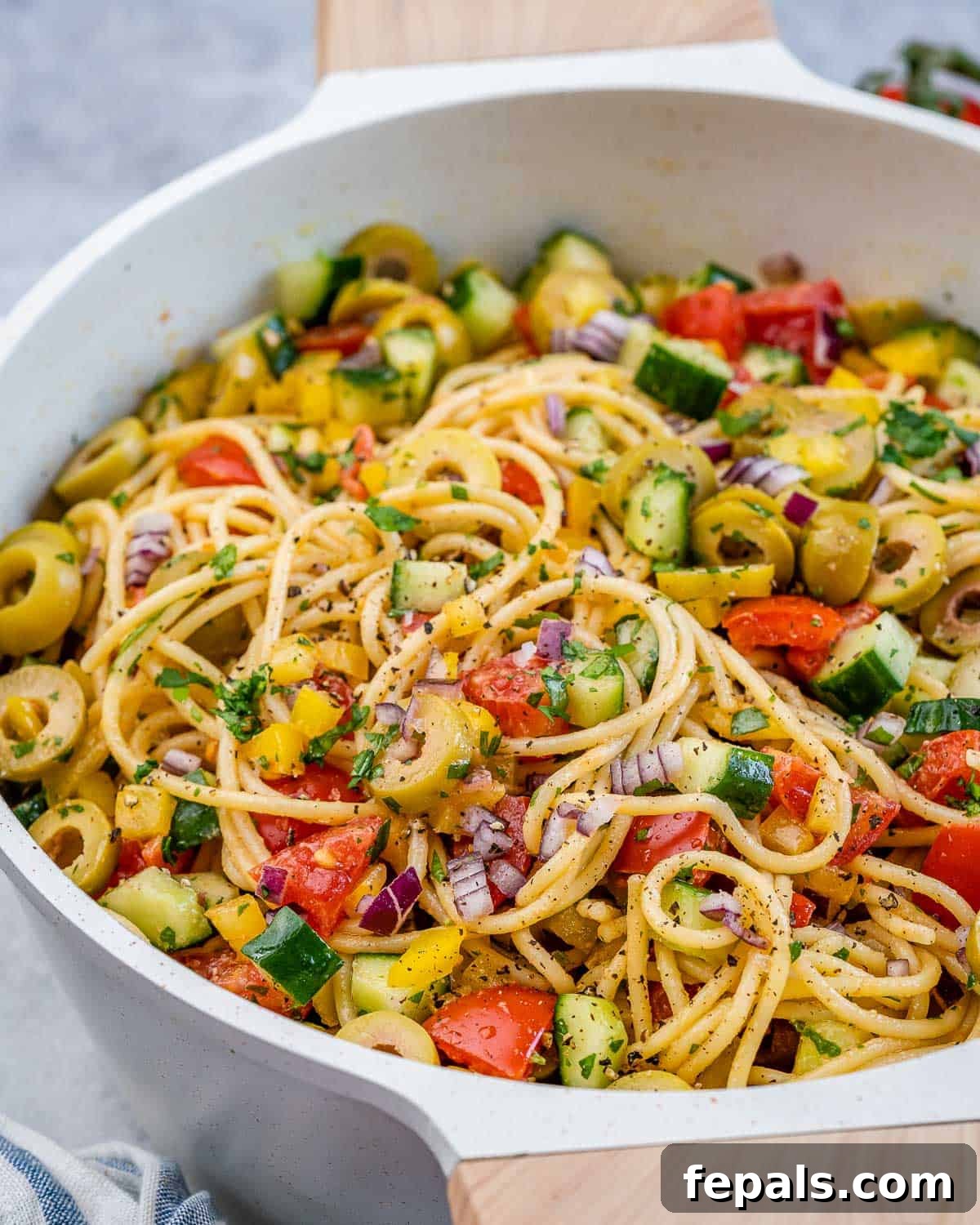 Refreshing Spaghetti Salad 8 A close-up shot of a refreshing spaghetti salad served in a elegant white dish, showcasing the perfect blend of long pasta strands, colorful diced vegetables, and savory olives.