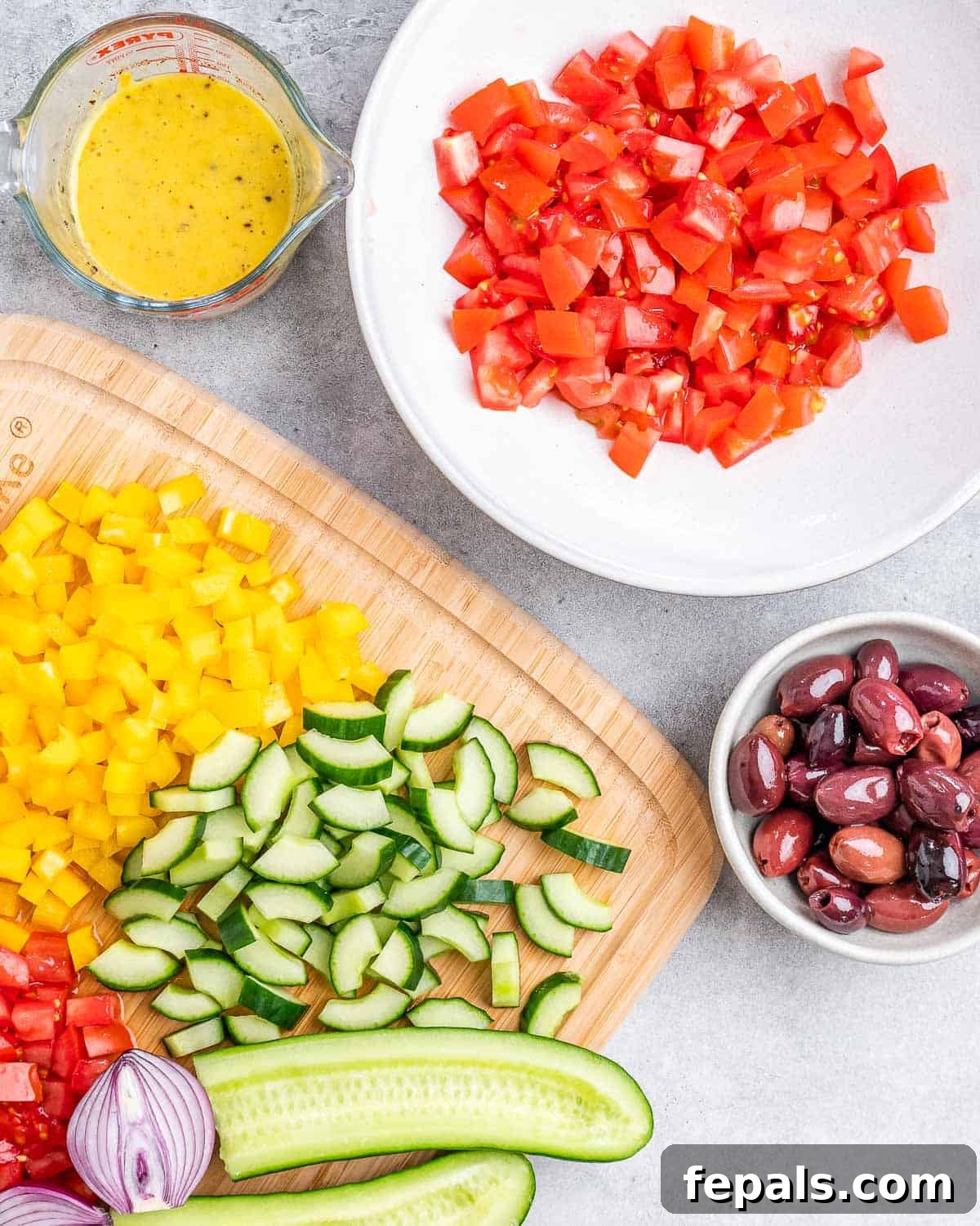A bowl filled with freshly chopped tomatoes, accompanied by diced cucumber, sliced olives, and finely chopped yellow bell pepper, ready for the salad.