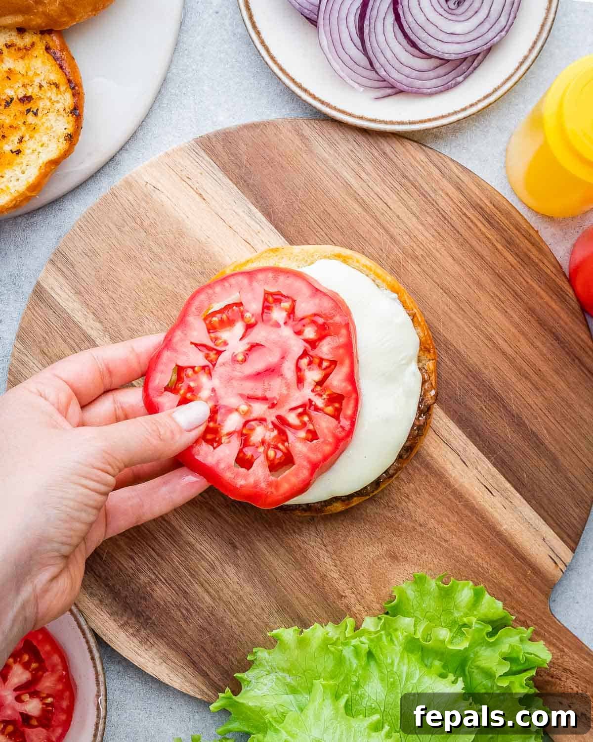 Burger Perfection, Made Easy 8 Adding a tomato slice over a bun with cheese.