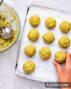 Baking sheet lined with parchment paper holding uncooked falafel balls before frying.