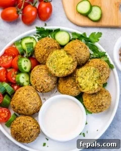 Platter of falafel balls with fresh vegetables and a bowl of creamy tahini sauce for dipping.