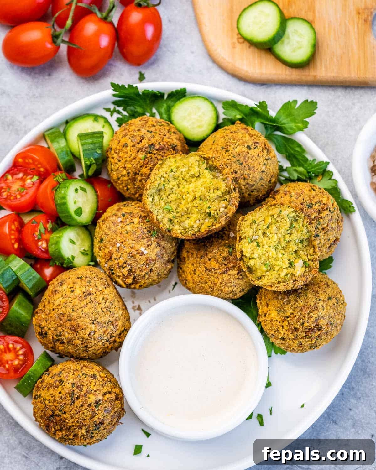 Crispy Homemade Falafel Made Simple 6 Platter of falafel balls with fresh vegetables and a bowl of creamy tahini sauce for dipping.