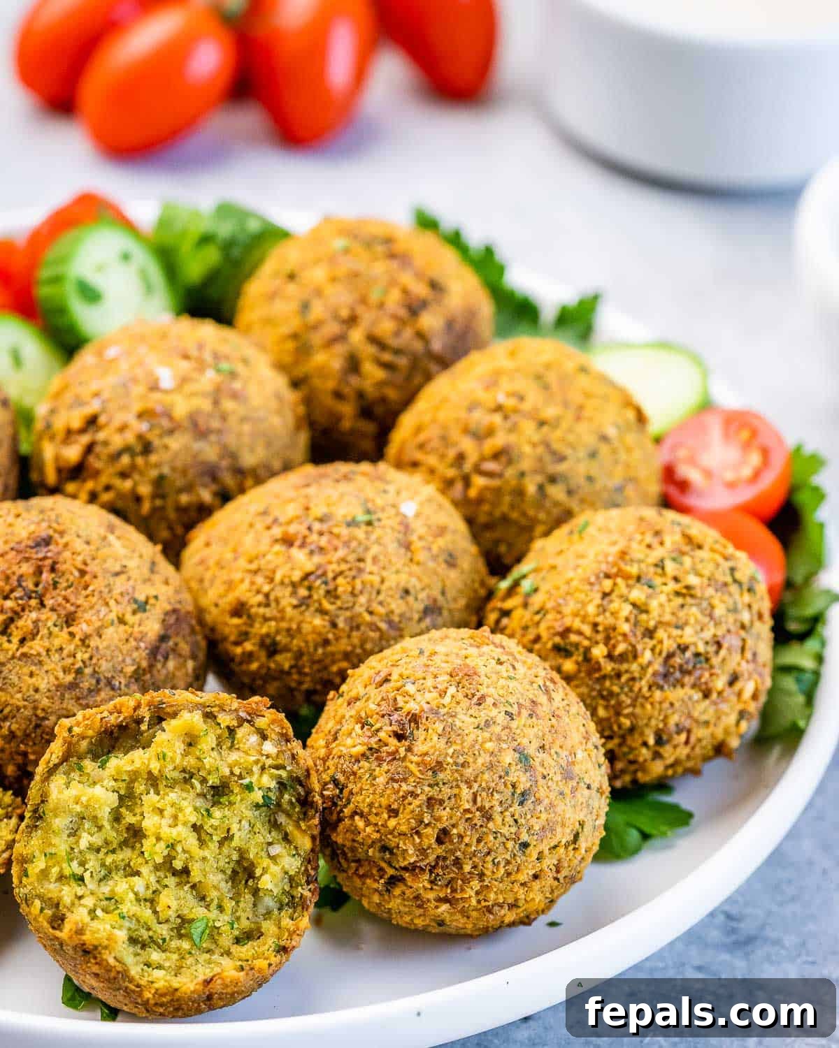 Crispy Homemade Falafel Made Simple 7 Close-up of golden-brown fried falafel balls piled on a plate with fresh cucumber and tomato slices.