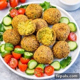 Crispy Homemade Falafel Made Simple 8 Freshly fried falafel balls on a plate with cucumber slices, cherry tomatoes, and parsley garnish.