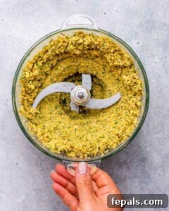 Food processor bowl filled with ground chickpea and herb mixture for making falafel.