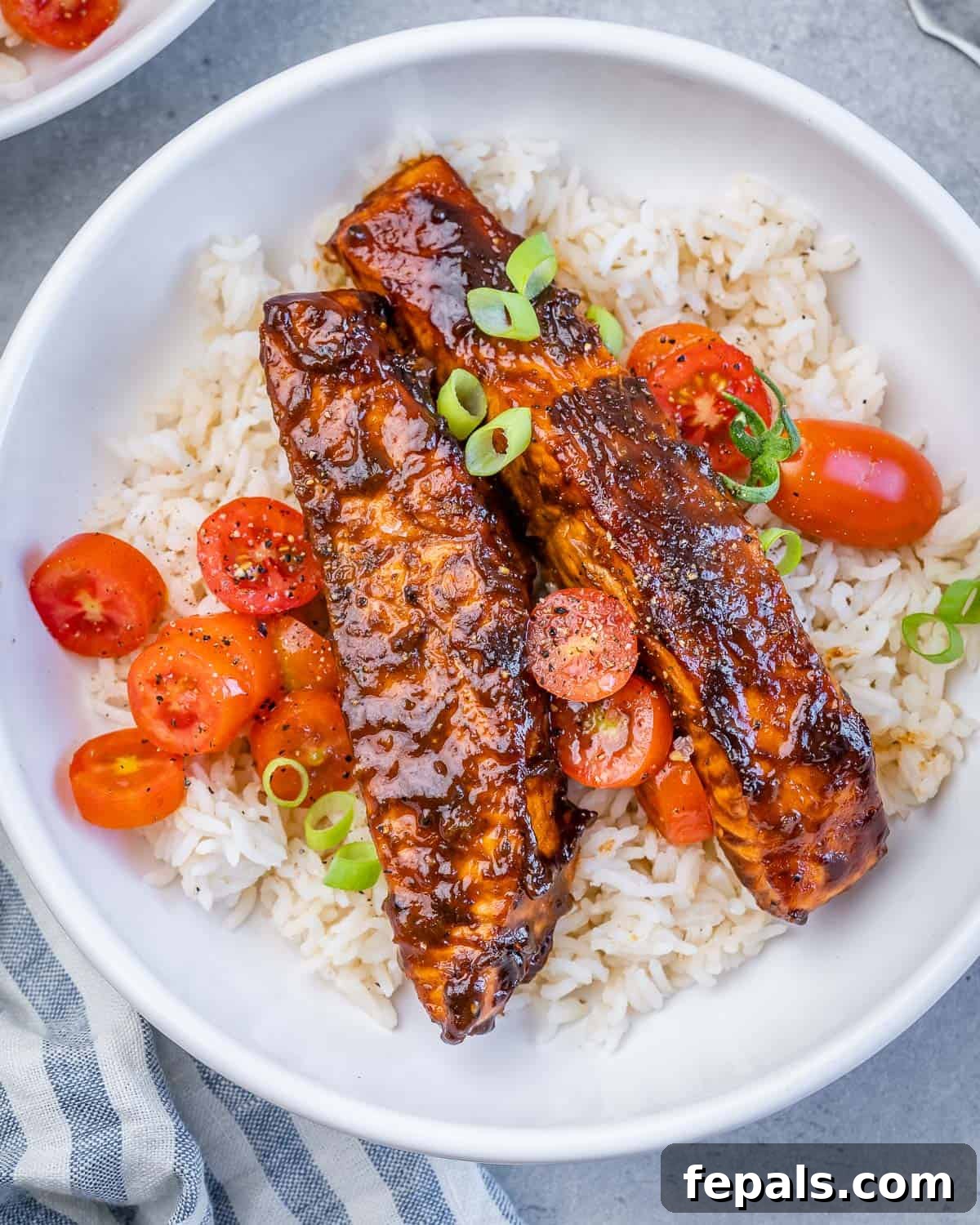 A white bowl with rice topped with 2 salmon fillets and tomato salad garnish.