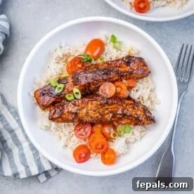 A white bowl with rice topped with 2 salmon fillets and tomato salad garnish.