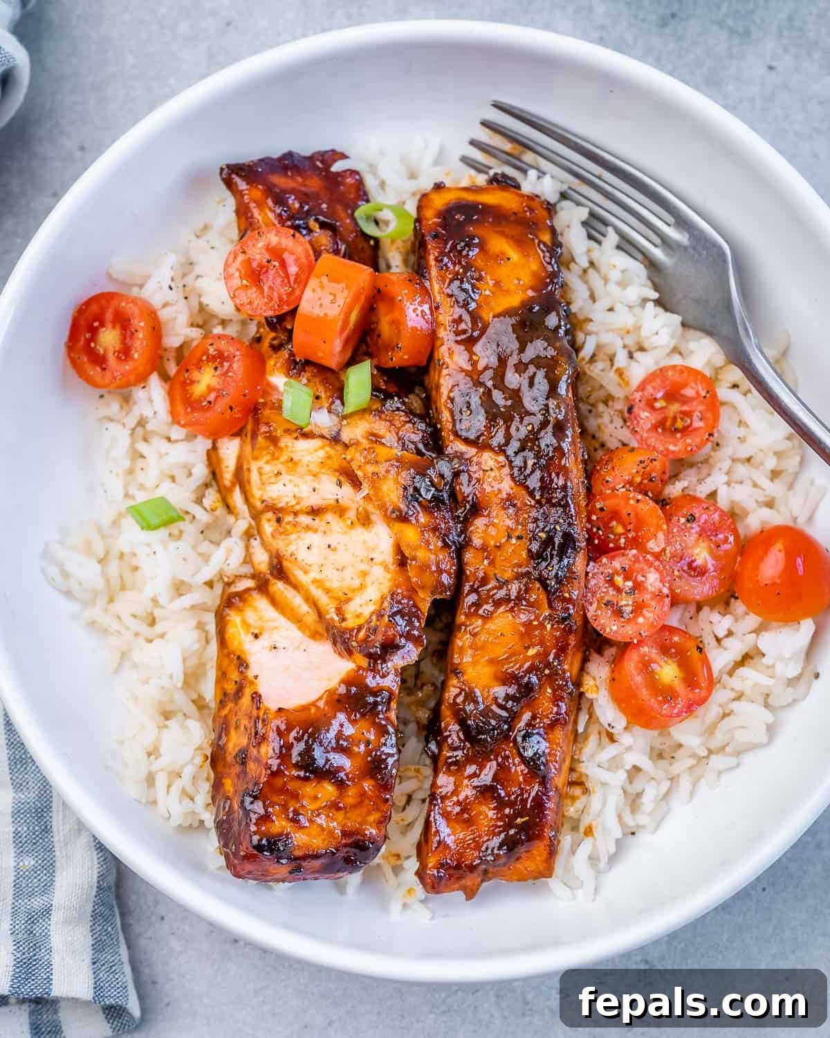 Flaked balsamic glazed salmon in a bowl with rice and cherry tomatoes.