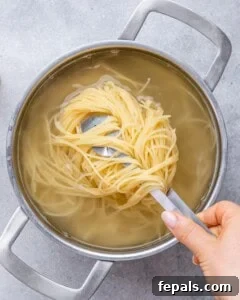 Hand lifting a portion of cooked spaghetti out of a pot of boiling water using kitchen tongs.