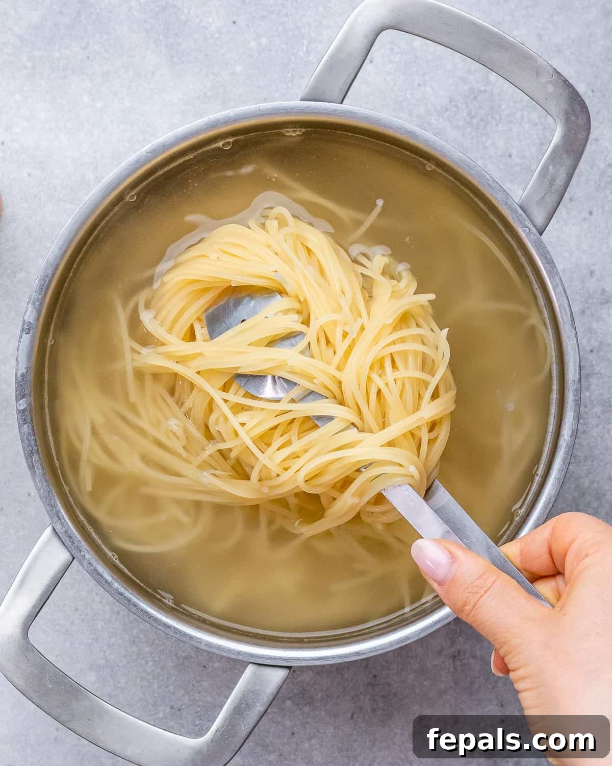 Velvety Cottage Cheese Alfredo 4 Hand lifting a portion of cooked spaghetti out of a pot of boiling water using kitchen tongs.