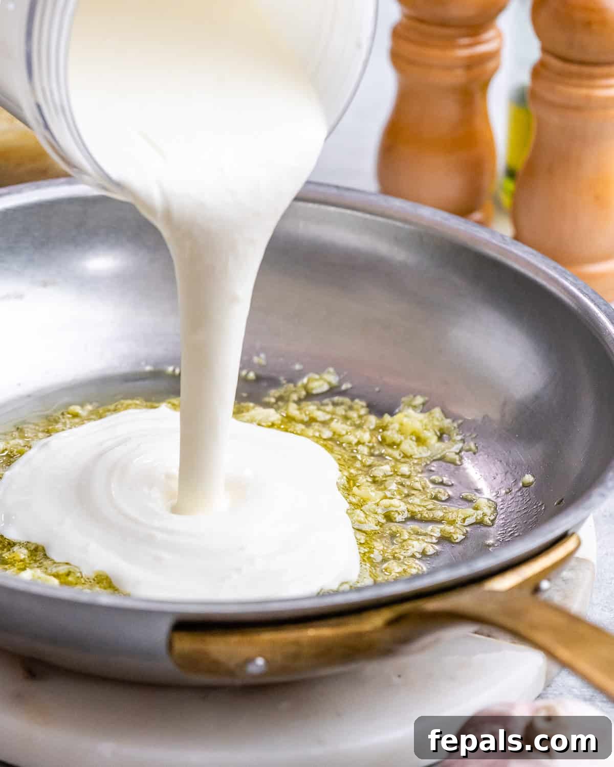Velvety Cottage Cheese Alfredo 6 Sauce streaming into the hot skillet, mixing with the garlic and olive oil to begin thickening.