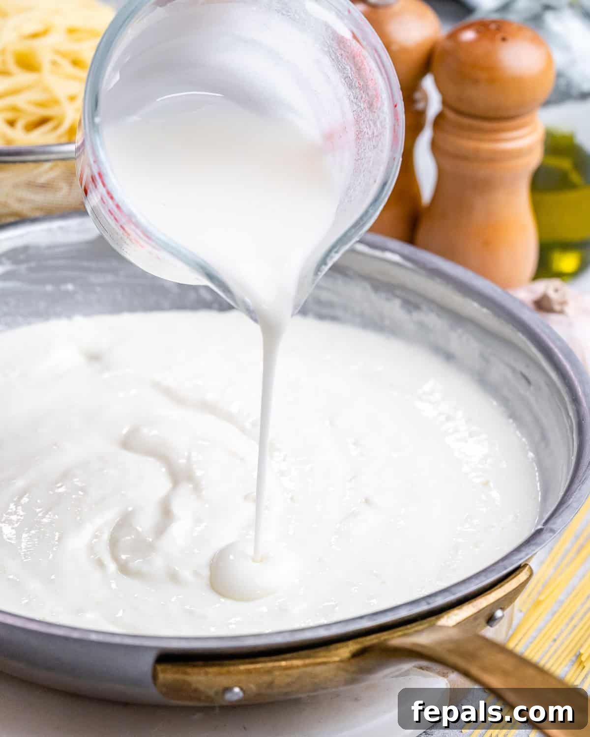 Velvety Cottage Cheese Alfredo 7 Thick cottage cheese Alfredo sauce being poured from a measuring cup into a skillet with sautéed garlic.
