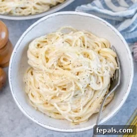 White bowl filled with spaghetti mixed with Alfredo sauce, showing smooth and creamy texture.