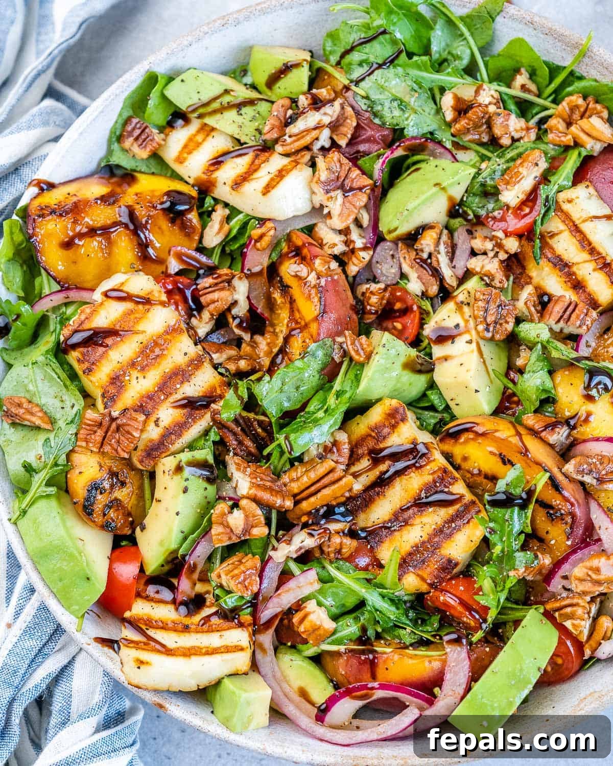Shot of grilled peach and halloumi salad topped with chopped pecans and balsamic glaze. A vibrant and appealing summer salad.