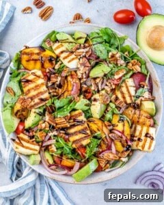Summer salad with grilled peaches, sliced avocado, halloumi, red onion, cherry tomatoes, and pecans on mixed greens.