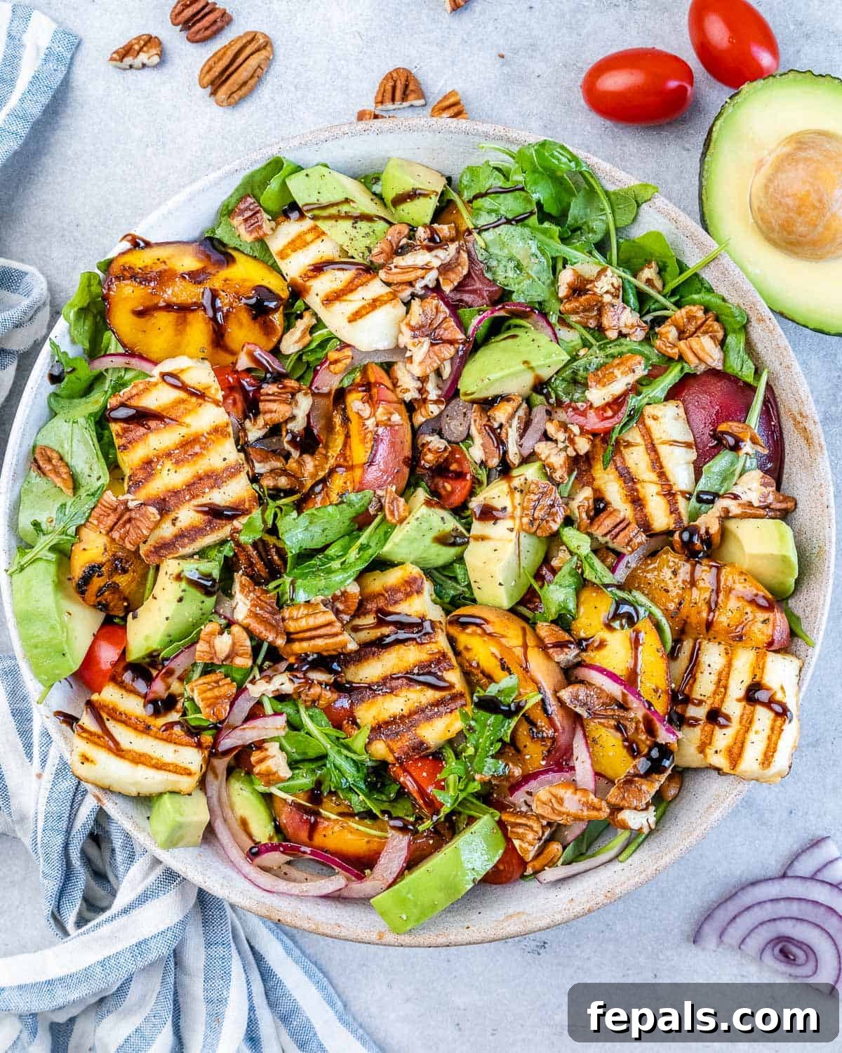 Summer salad with grilled peaches, sliced avocado, halloumi, red onion, cherry tomatoes, and pecans on mixed greens, beautifully plated.