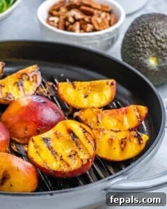 Close-up of grilled peach halves on a grill pan, developing dark charred grill marks.