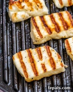 Halloumi slices grilling on a pan with golden brown grill marks.