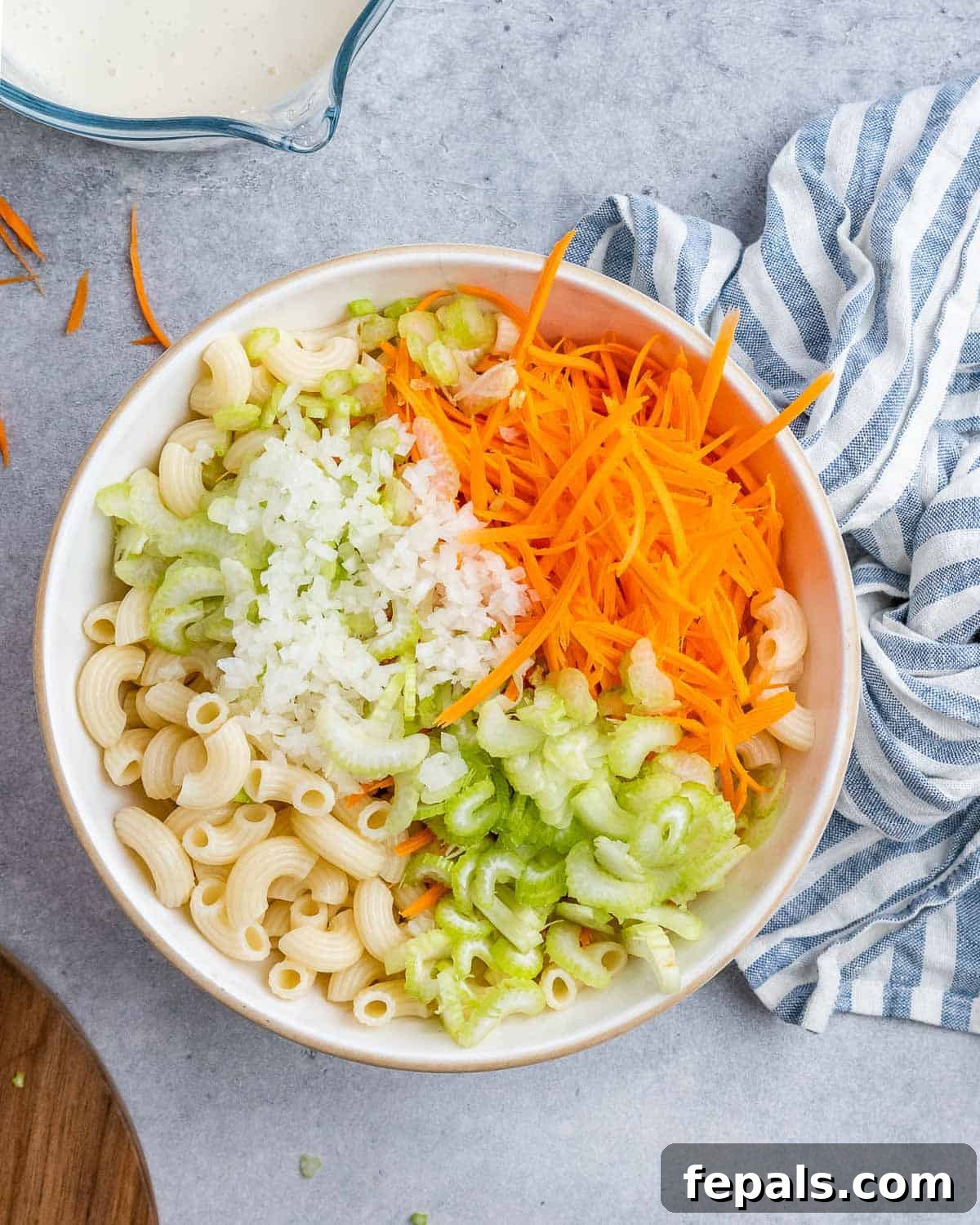 Aloha Macaroni Salad 7 The vibrant components of Hawaiian mac salad – fluffy elbow macaroni, bright grated carrots, crisp chopped celery, and aromatic grated onion – artfully arranged in a large mixing bowl, poised for the creamy dressing.