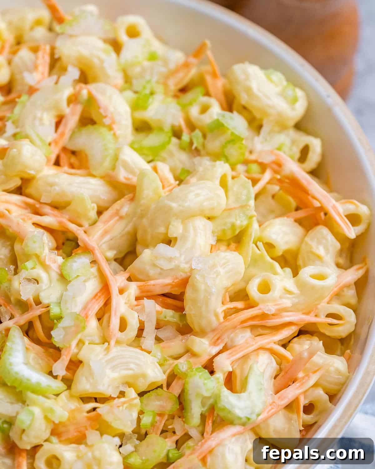 Aloha Macaroni Salad 9 A zoomed-in, mouth-watering view of the finished macaroni salad, highlighting the perfectly coated pasta with creamy dressing, intertwined with finely shredded carrots and crisp chopped celery, demonstrating its appetizing texture and vibrant colors.