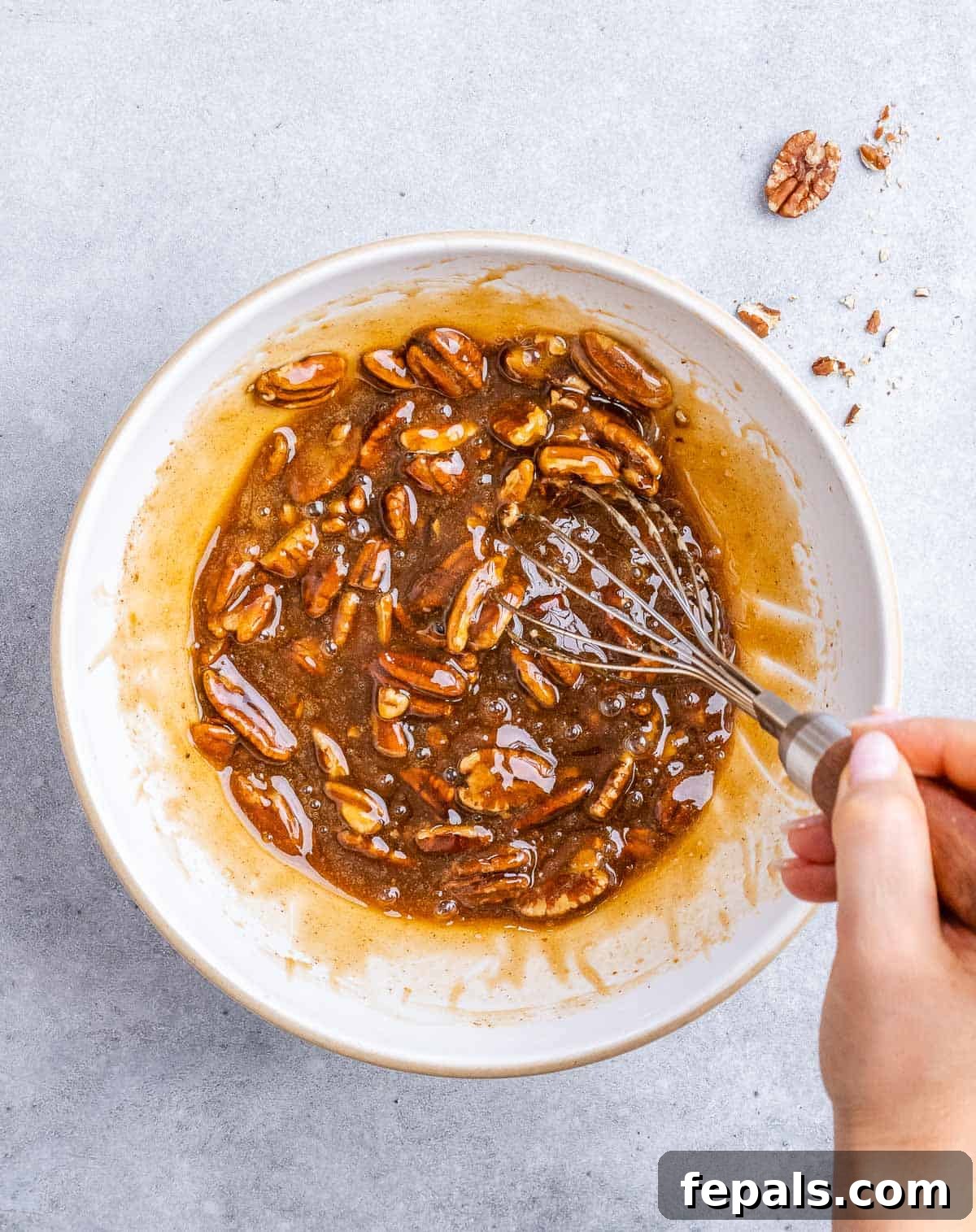 Stirring pecans with honey, egg, sugar mixture in a white bowl.