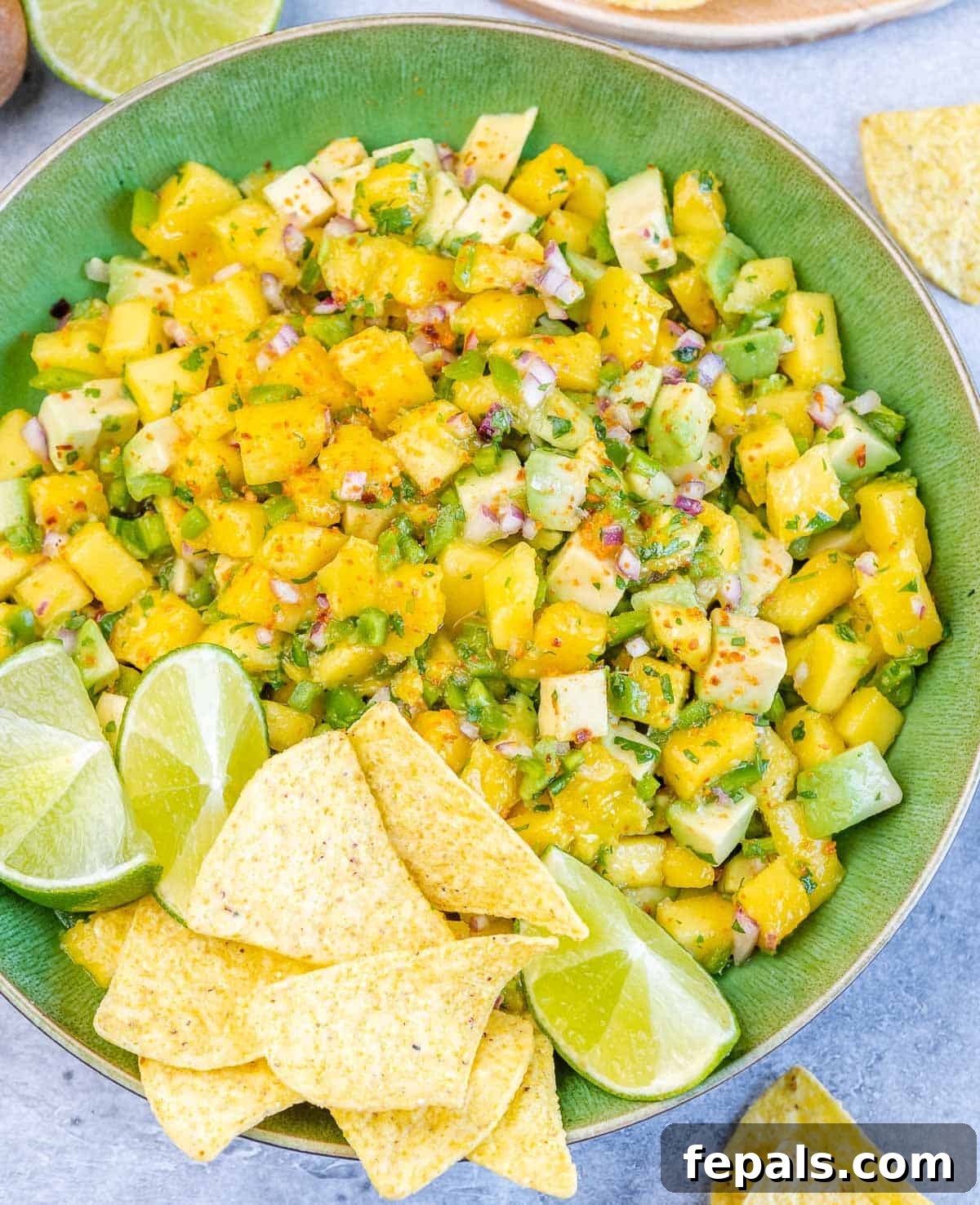 Mango salsa in a green bowl, accompanied by tortilla chips and lime wedges, showcasing its serving potential.
