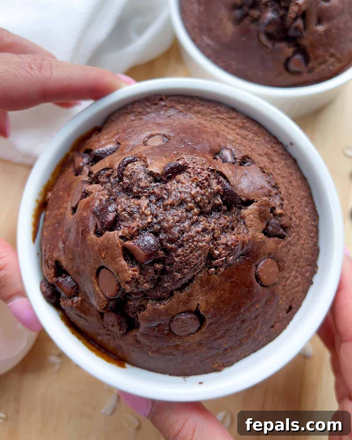 Decadent Chocolate Protein Baked Oats 2 Hand holding a ramekin with rich chocolate protein baked oats, resembling a mini brownie cake.
