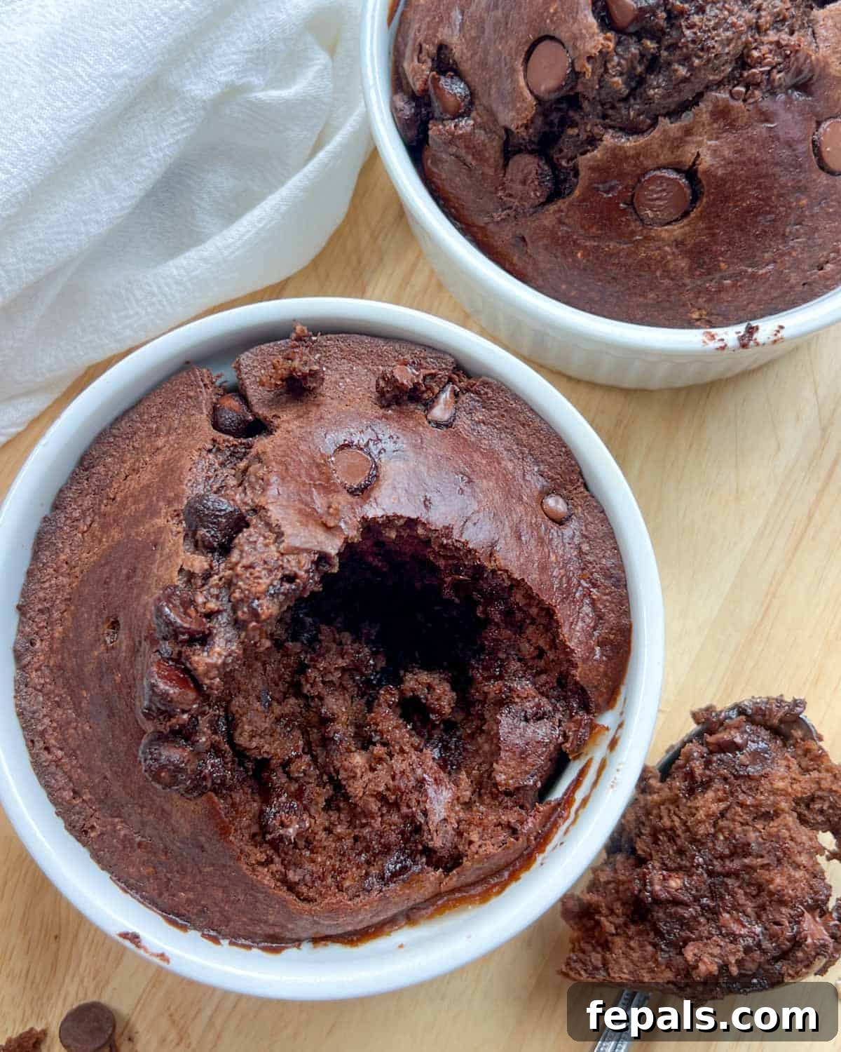 Decadent Chocolate Protein Baked Oats 11 A portion of chocolate baked oats is scooped out of the ramekin and placed on a flat surface next to the bowl.