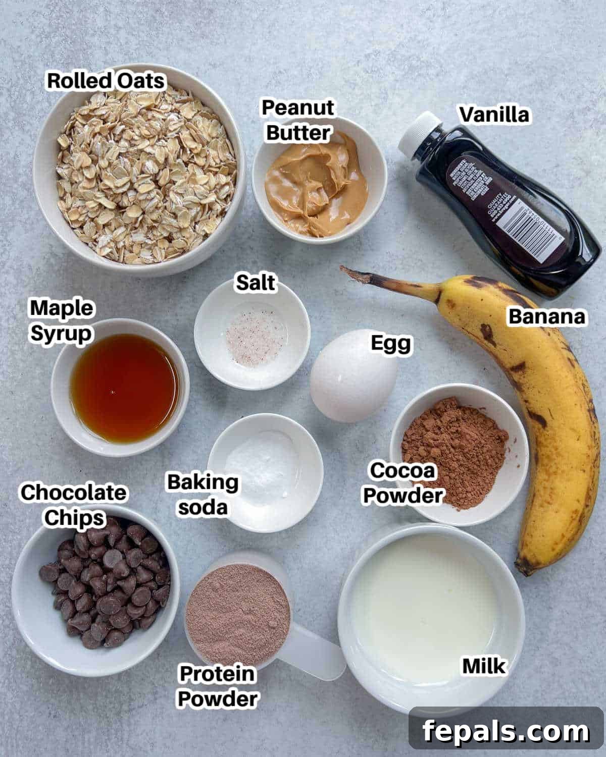 Decadent Chocolate Protein Baked Oats 3 Ingredients to make protein baked oats laid out on a flat surface, showcasing oats, banana, egg, milk, cocoa, protein powder, and chocolate chips.