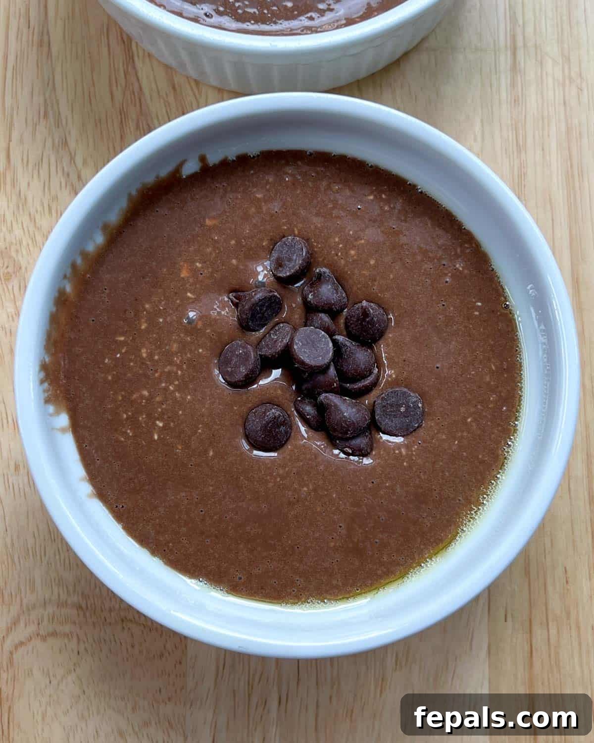 Decadent Chocolate Protein Baked Oats 6 Chocolate batter is poured into a prepared ramekin and topped with a scattering of chocolate chips.