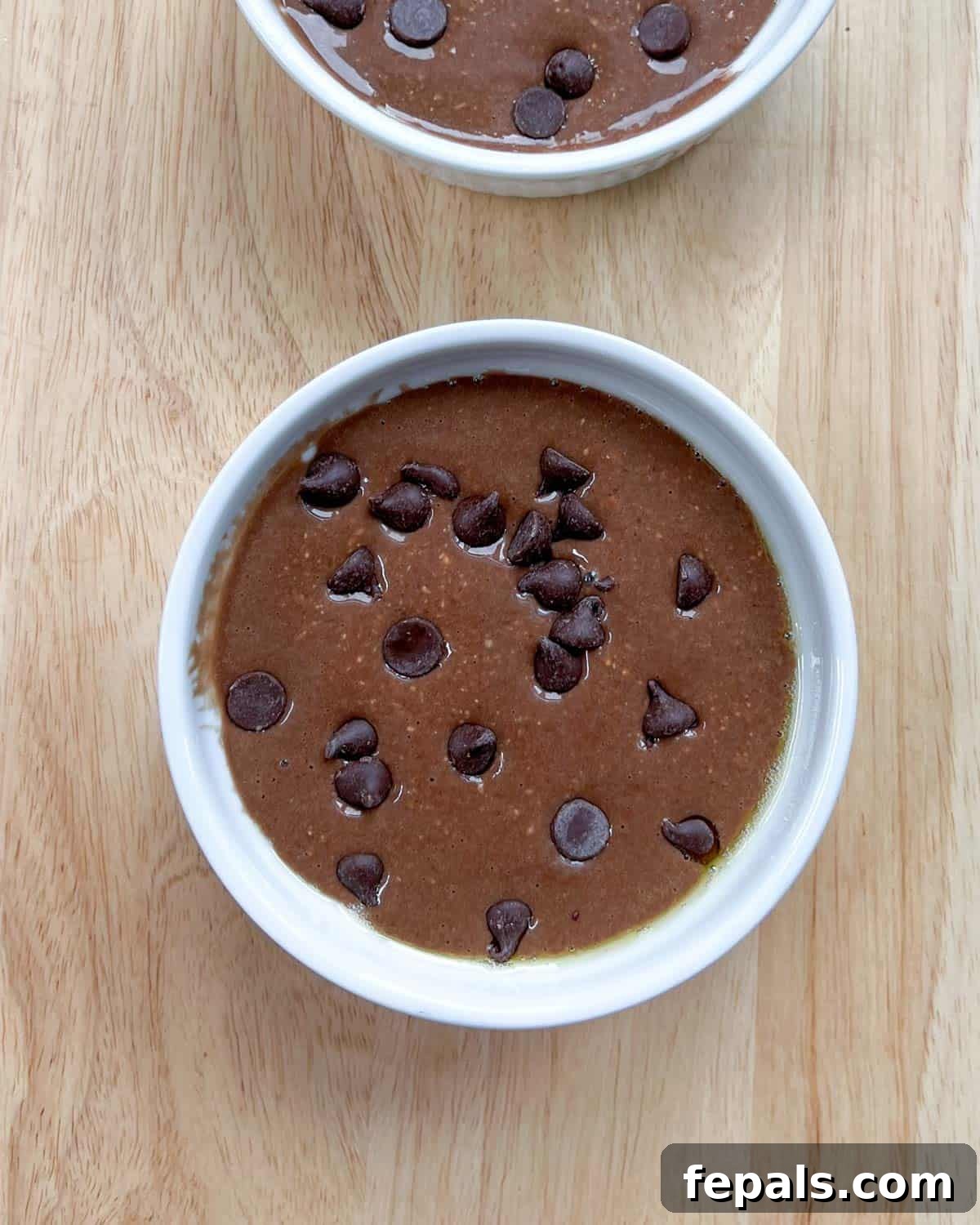 Decadent Chocolate Protein Baked Oats 7 The chocolate batter in the ramekin is shown with mixed-in chocolate chips and a fresh layer of chips on top.